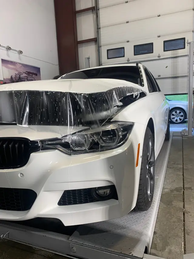 White BMW on the lift with clear film laid over the front end