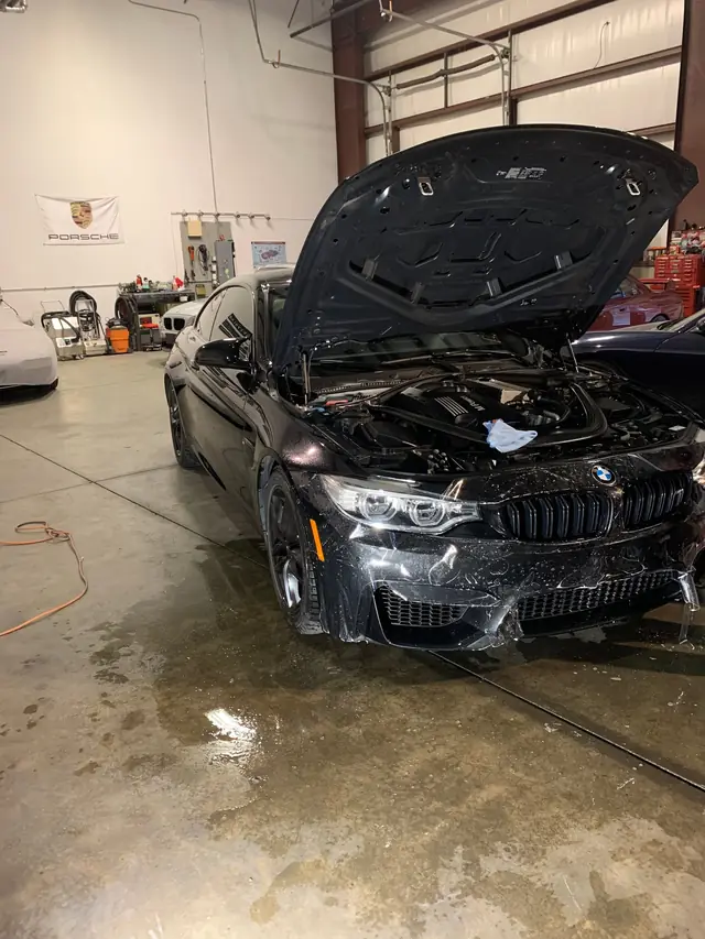 Black BMW with the hood up on a wet wash-bay floor
