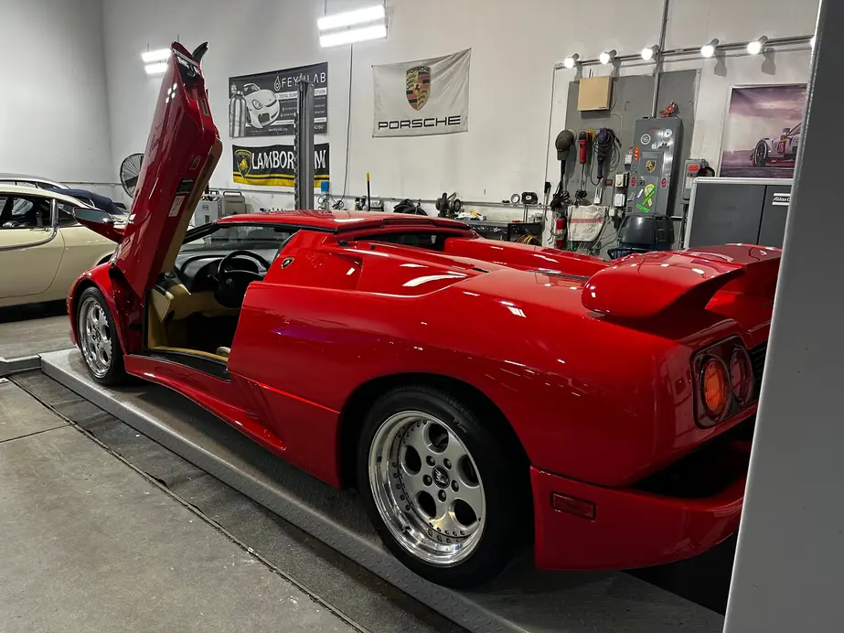 Red Lamborghini roadster raised on the two-post lift inside the shop