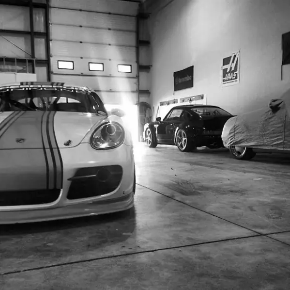 White Porsche Cayman with black stripes, a car under cover behind it